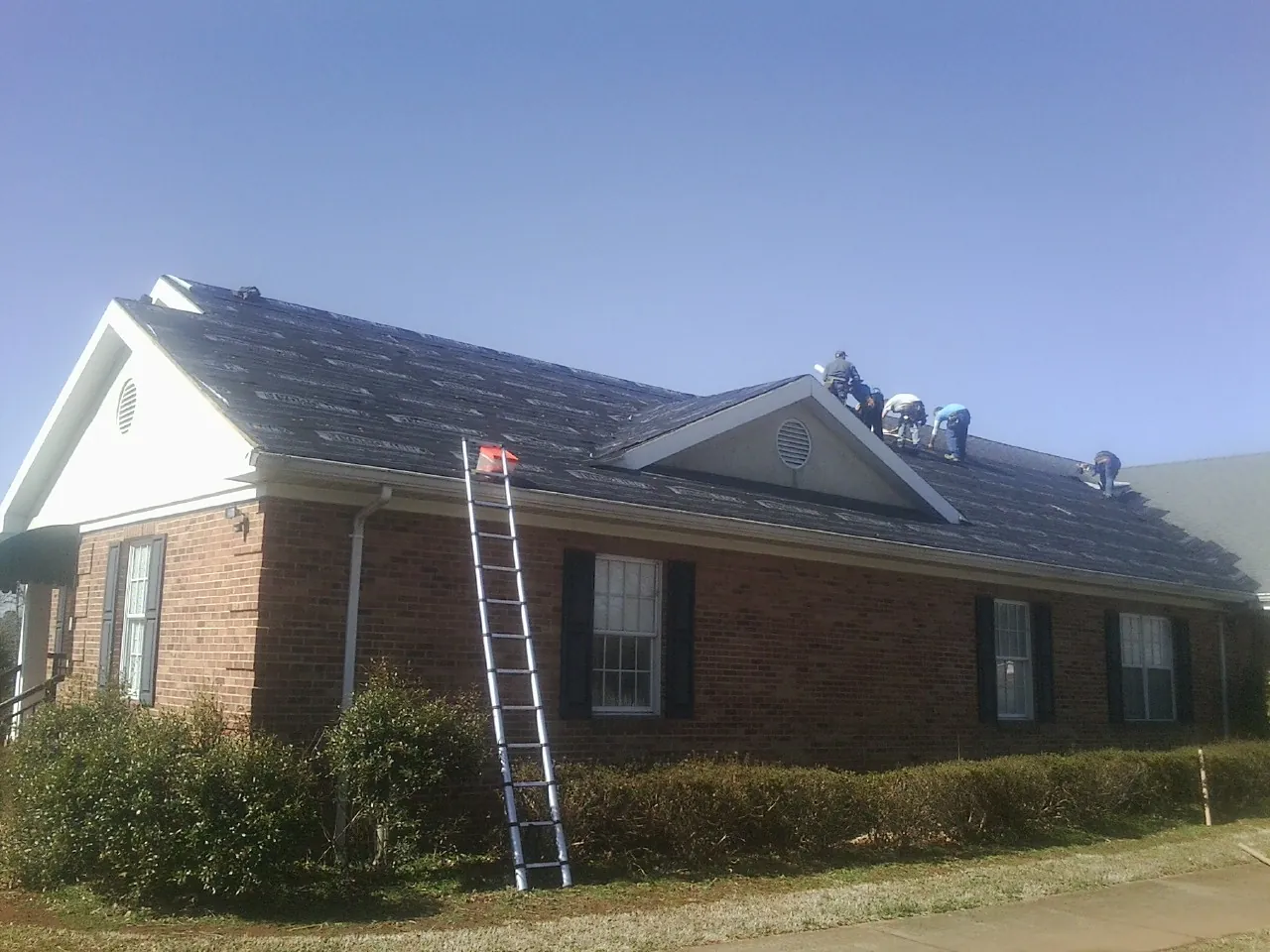 Crew tearing shingles off a brick ranch roof with a ladder set — Metal Roof Repair work by our crew in Glenwood